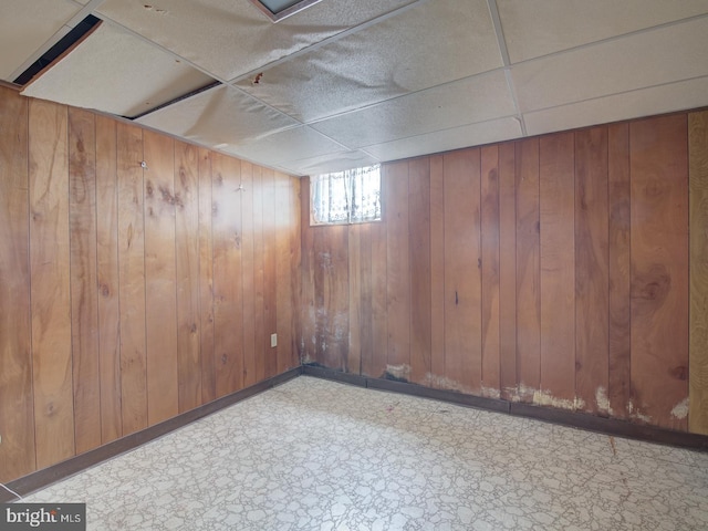 basement with a paneled ceiling and wood walls