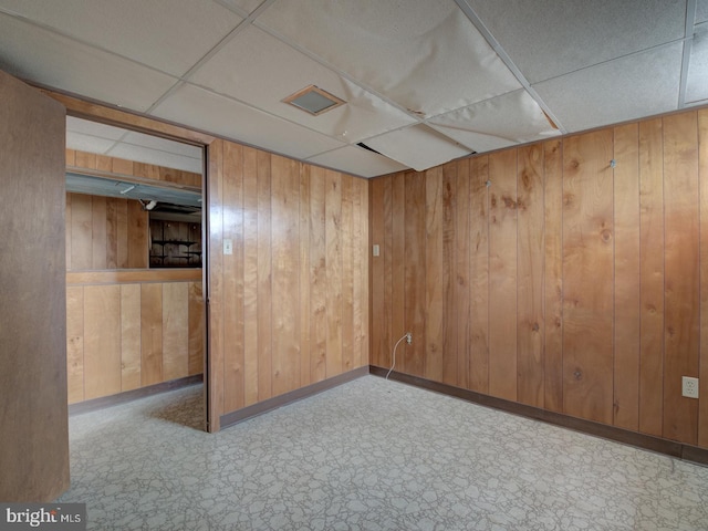 empty room featuring a paneled ceiling and wooden walls