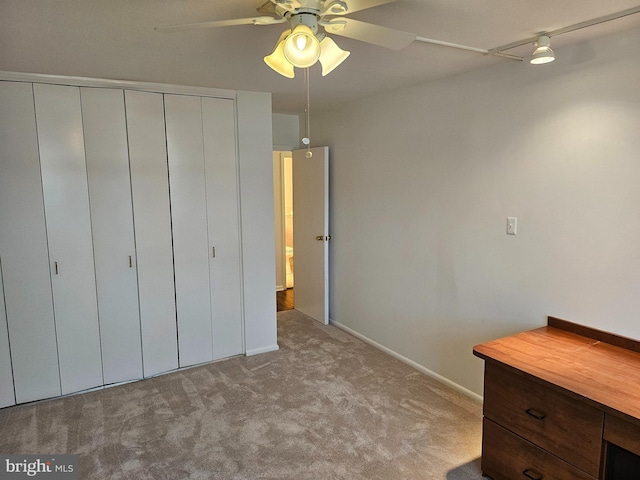 unfurnished bedroom featuring a closet, light colored carpet, track lighting, and ceiling fan