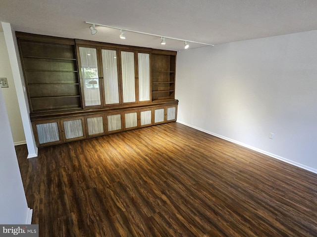 spare room with a textured ceiling, rail lighting, and dark hardwood / wood-style floors