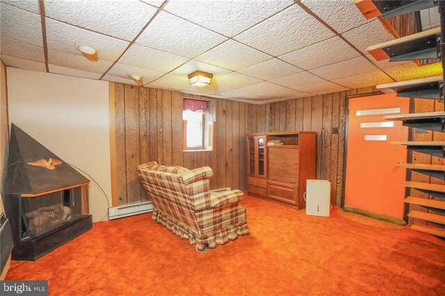 unfurnished room featuring carpet flooring, baseboard heating, and wood walls