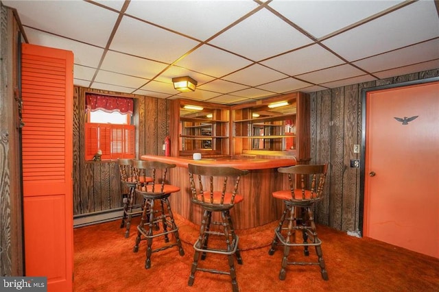 bar with carpet, a drop ceiling, baseboard heating, and wooden walls