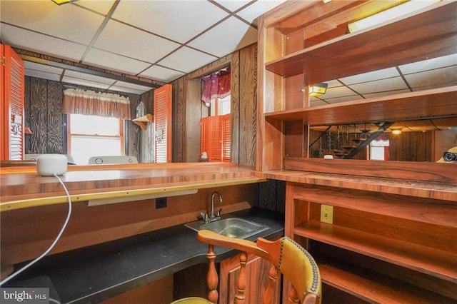 bar with a drop ceiling, wooden walls, and sink