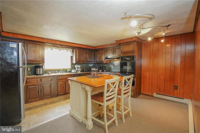 kitchen with a baseboard heating unit, backsplash, a breakfast bar, a kitchen island, and black appliances