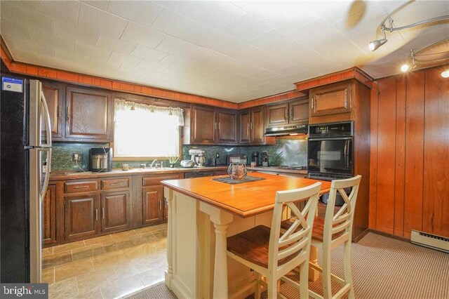 kitchen with decorative backsplash, a baseboard radiator, a breakfast bar area, oven, and stainless steel refrigerator