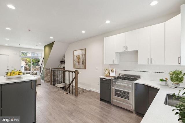 kitchen with light wood-type flooring, high end stove, white cabinets, and backsplash