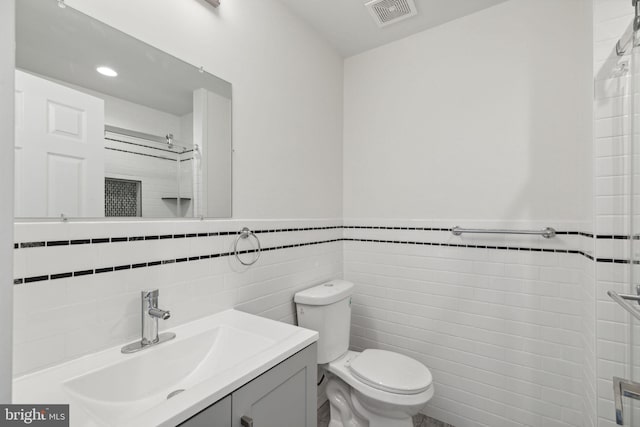 bathroom with vanity, toilet, and tile walls