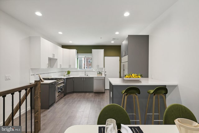 kitchen with sink, light hardwood / wood-style flooring, gray cabinets, premium appliances, and white cabinetry