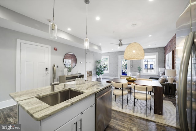 kitchen featuring pendant lighting, a center island with sink, light stone countertops, appliances with stainless steel finishes, and white cabinetry