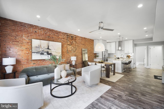 living room featuring sink, hardwood / wood-style flooring, ceiling fan, and brick wall