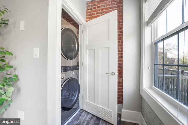 laundry room featuring stacked washing maching and dryer, dark hardwood / wood-style floors, and brick wall