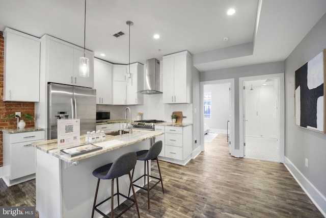 kitchen featuring wall chimney exhaust hood, stainless steel appliances, dark hardwood / wood-style flooring, an island with sink, and white cabinets