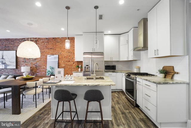 kitchen featuring wall chimney exhaust hood, hanging light fixtures, dark wood-type flooring, white cabinets, and appliances with stainless steel finishes