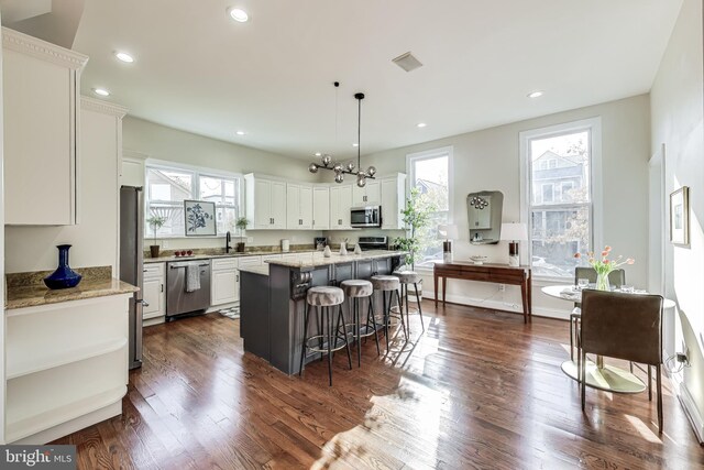 kitchen with a breakfast bar, a center island, white cabinets, hanging light fixtures, and stainless steel appliances