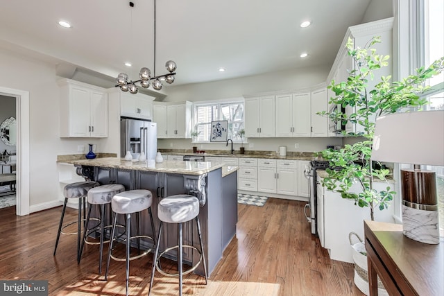 kitchen with white cabinetry, stainless steel appliances, light stone counters, pendant lighting, and a kitchen island