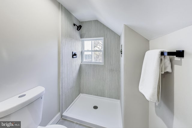 bathroom with toilet, tiled shower, and vaulted ceiling