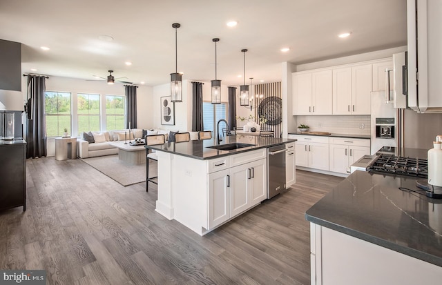 kitchen with appliances with stainless steel finishes, white cabinetry, dark wood-type flooring, and an island with sink