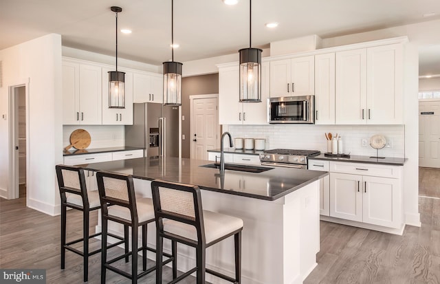 kitchen with high quality appliances, a kitchen island with sink, sink, light wood-type flooring, and white cabinetry