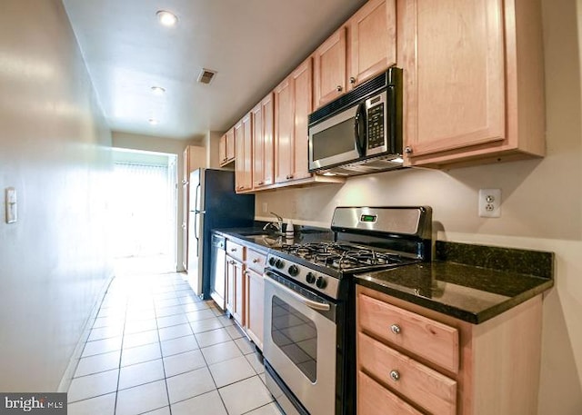 kitchen featuring dark stone counters, sink, light tile patterned floors, light brown cabinetry, and appliances with stainless steel finishes