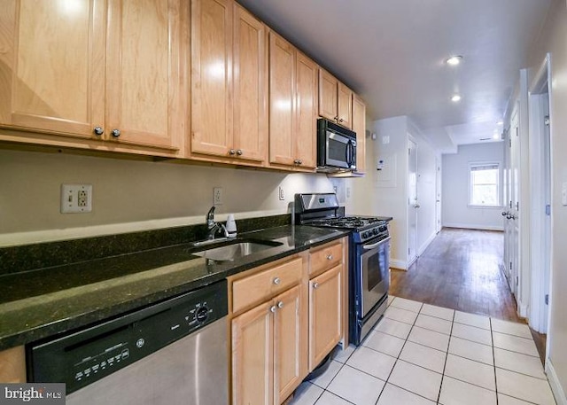 kitchen with sink, light tile patterned floors, stainless steel appliances, and dark stone counters