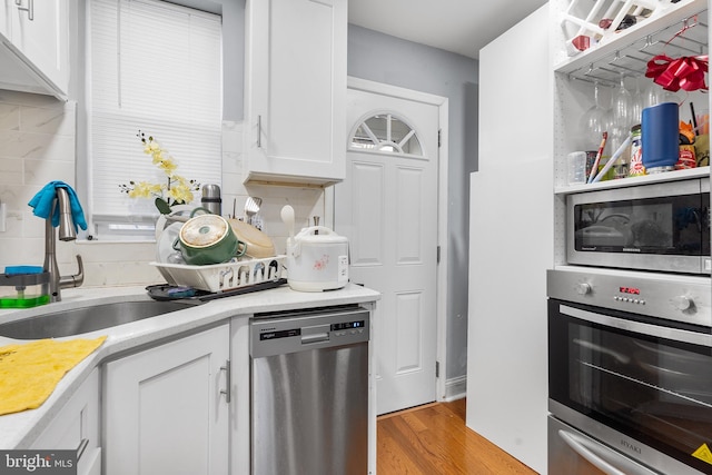 kitchen featuring tasteful backsplash, stainless steel appliances, sink, white cabinets, and light hardwood / wood-style floors