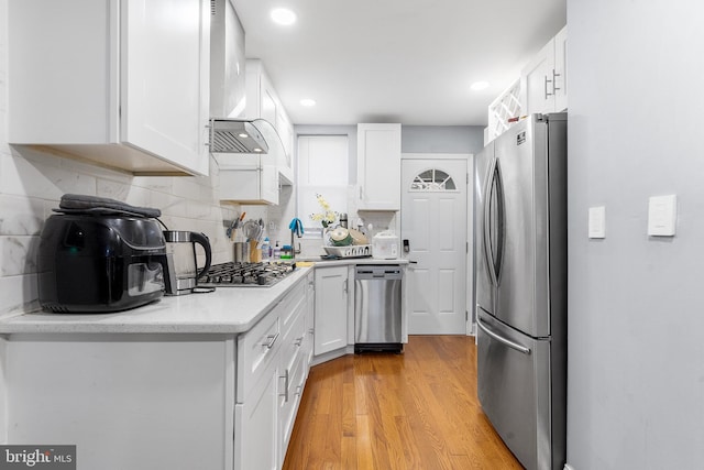 kitchen with light wood-type flooring, stainless steel appliances, white cabinetry, and tasteful backsplash