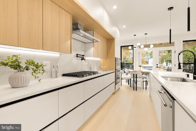 kitchen featuring white cabinetry, sink, wall chimney range hood, decorative light fixtures, and appliances with stainless steel finishes