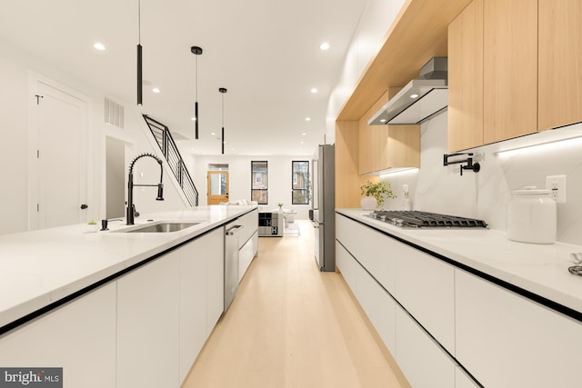 kitchen with sink, wall chimney exhaust hood, stainless steel appliances, hanging light fixtures, and white cabinets