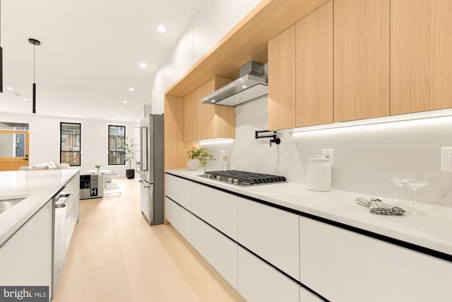 kitchen with white cabinets, wall chimney exhaust hood, pendant lighting, and appliances with stainless steel finishes