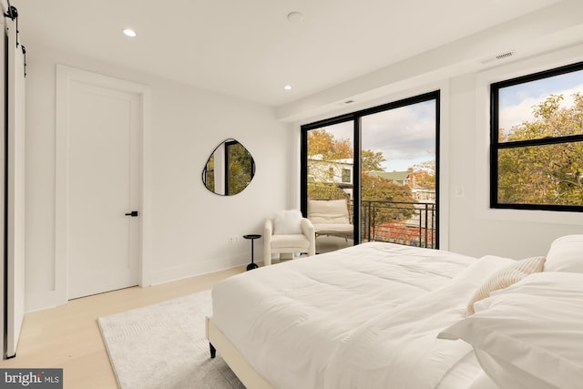 bedroom with a barn door, access to exterior, and light wood-type flooring