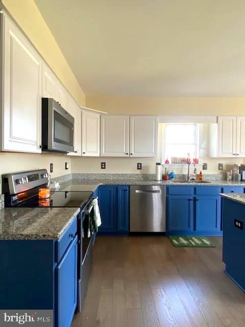 kitchen featuring dark wood-type flooring, stainless steel appliances, white cabinets, and blue cabinetry