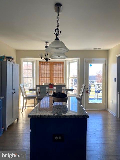 kitchen with a healthy amount of sunlight, wood-type flooring, decorative light fixtures, and dark stone countertops