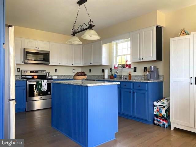 kitchen featuring blue cabinetry, a kitchen island, pendant lighting, stainless steel appliances, and white cabinets