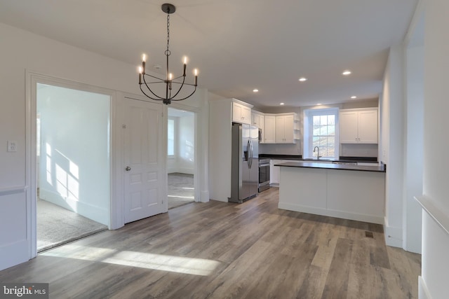 kitchen featuring light wood-type flooring, stainless steel appliances, a notable chandelier, white cabinetry, and hanging light fixtures