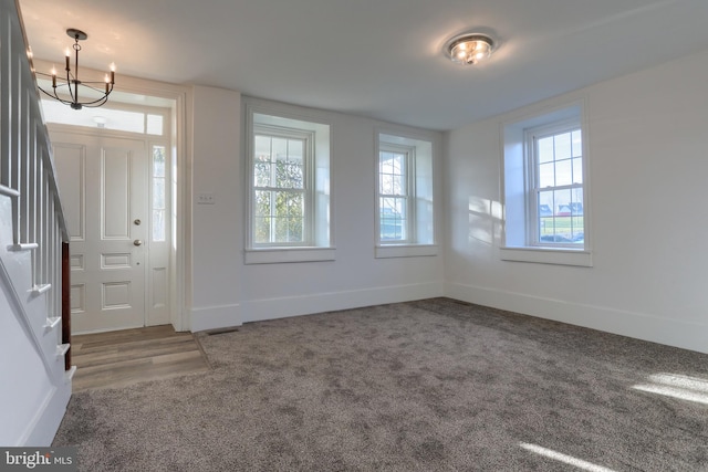 entrance foyer featuring an inviting chandelier, dark carpet, and a healthy amount of sunlight