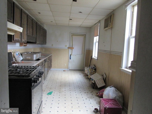 kitchen with an AC wall unit, stainless steel range with gas cooktop, a drop ceiling, and dark brown cabinets