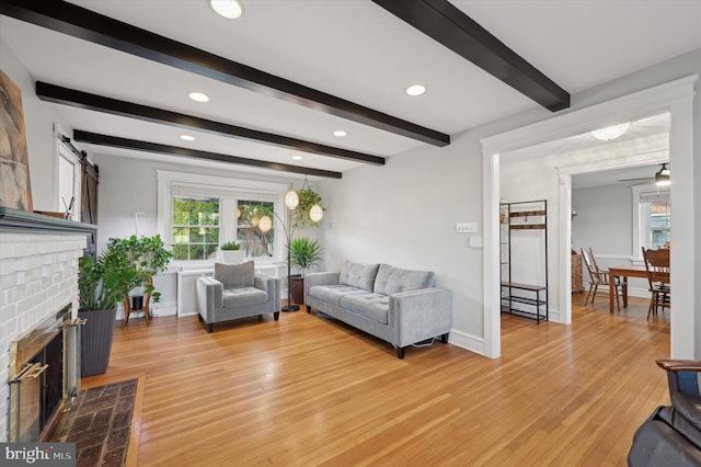 living room featuring beamed ceiling, light wood-type flooring, and a brick fireplace