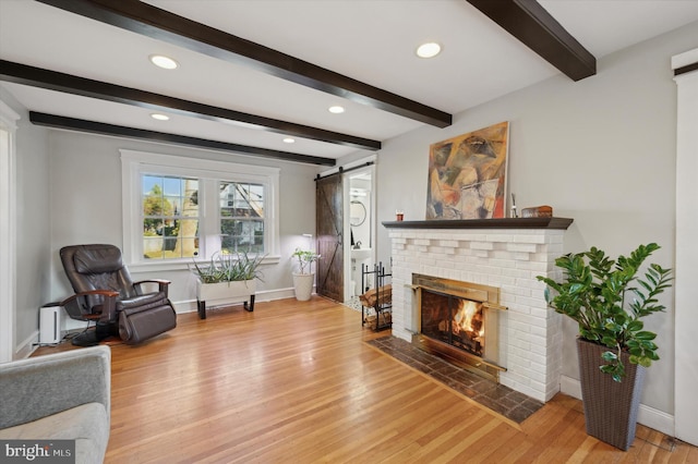 living room featuring hardwood / wood-style flooring, a barn door, beamed ceiling, and a brick fireplace