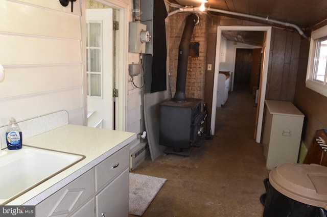 bathroom featuring wood walls, lofted ceiling, a wood stove, sink, and concrete flooring