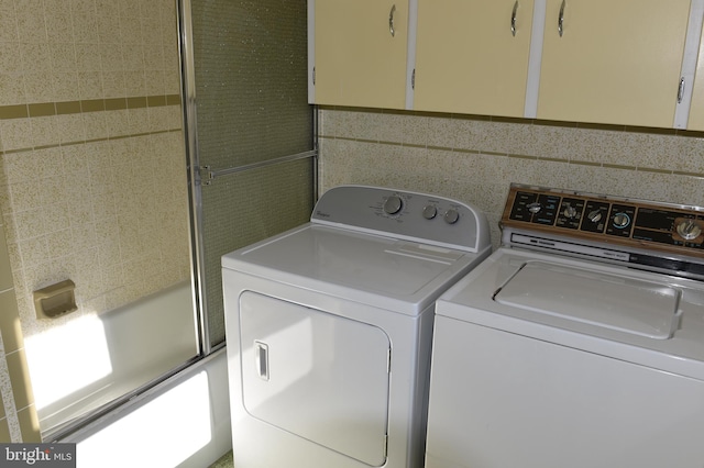 clothes washing area featuring washer and clothes dryer and tile walls