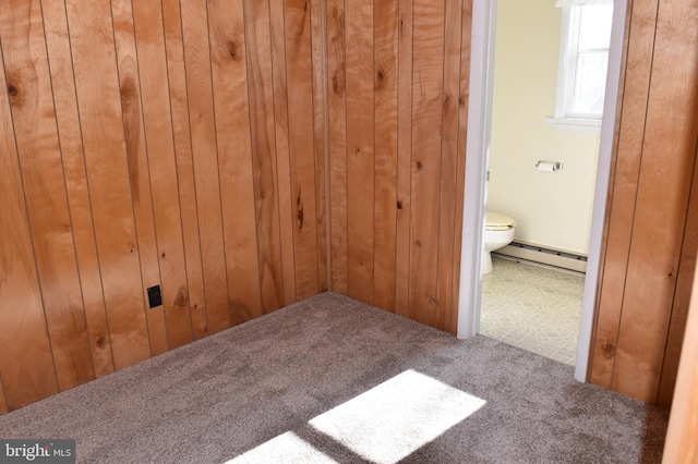 unfurnished bedroom featuring carpet flooring, connected bathroom, wooden walls, and a baseboard radiator