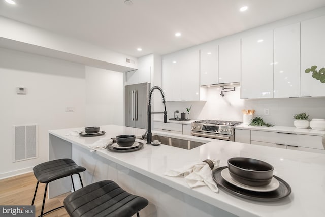 kitchen with white cabinetry, stainless steel range, light stone counters, light hardwood / wood-style floors, and a kitchen bar