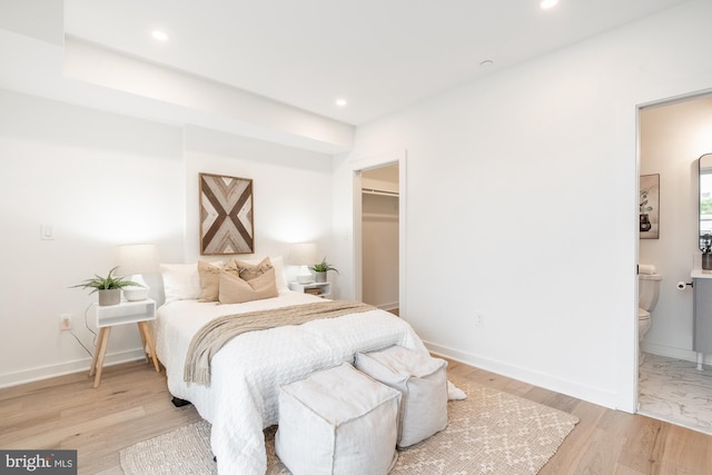 bedroom with ensuite bath, a walk in closet, and light hardwood / wood-style floors