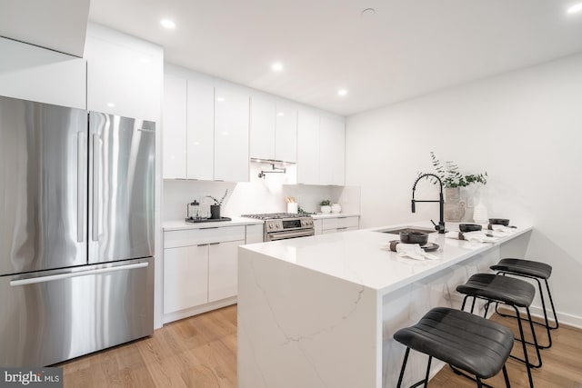 kitchen featuring a kitchen bar, white cabinetry, light hardwood / wood-style flooring, and appliances with stainless steel finishes