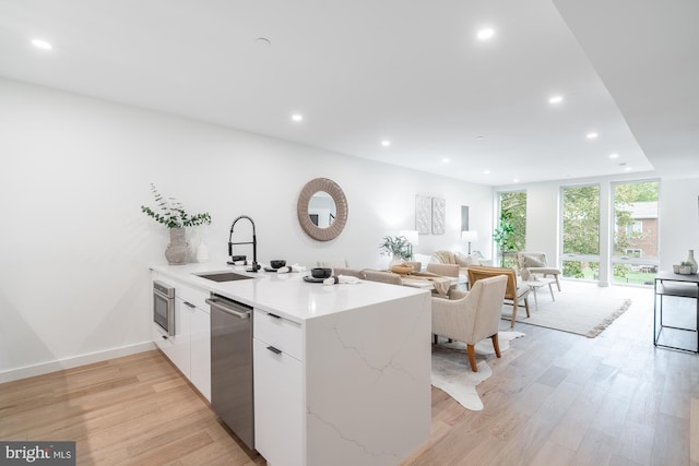 kitchen with kitchen peninsula, stainless steel appliances, sink, light hardwood / wood-style floors, and white cabinetry