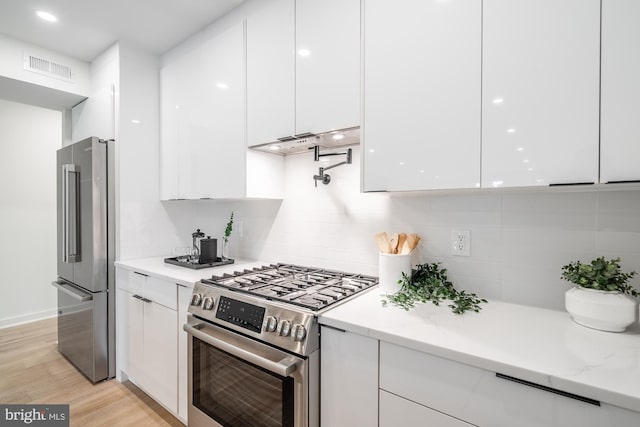 kitchen with decorative backsplash, appliances with stainless steel finishes, light stone counters, light hardwood / wood-style floors, and white cabinetry