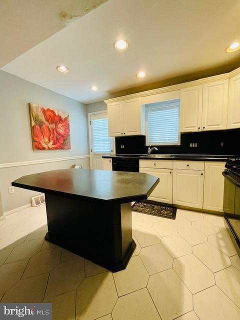 kitchen with a center island, range, light tile patterned floors, black dishwasher, and white cabinetry