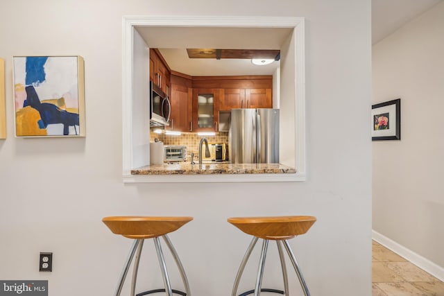 kitchen with decorative backsplash, appliances with stainless steel finishes, light stone counters, sink, and a breakfast bar area