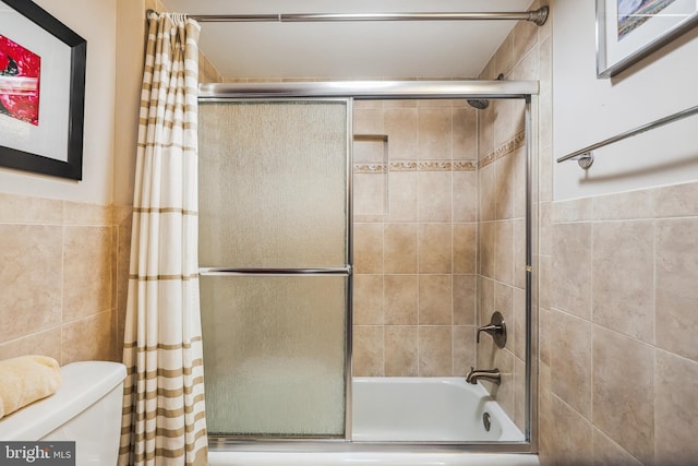 bathroom with shower / bath combination with glass door, toilet, and tile walls