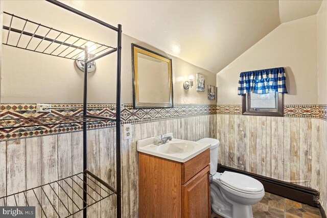 bathroom with toilet, vanity, vaulted ceiling, and tile walls